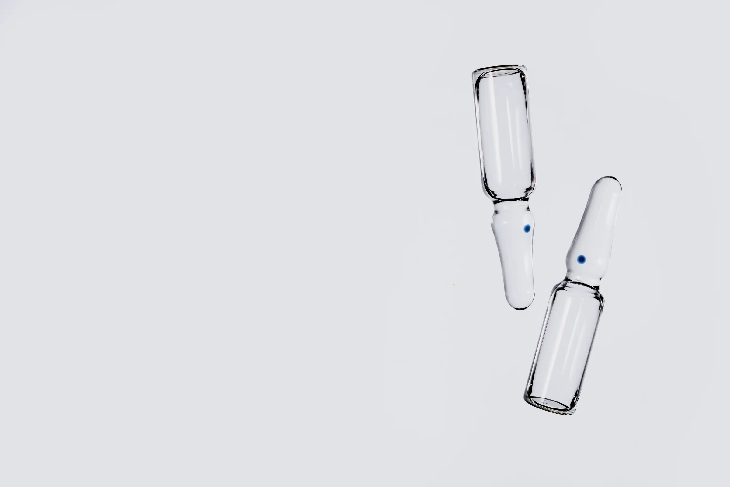 Two clear glass ampoules on a neutral surface